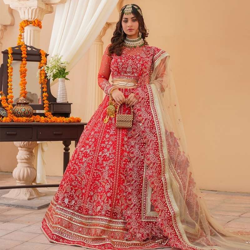 Woman in a red embroidered traditional outfit standing indoors with decorative elements.